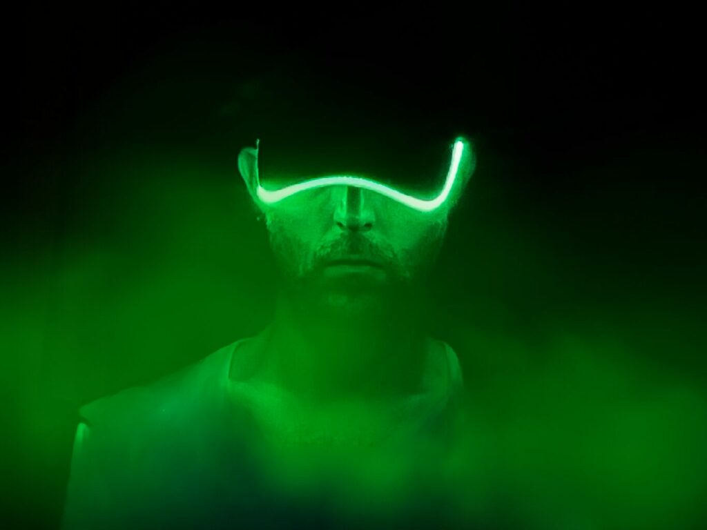 Il volto di un giovane uomo, il cappellino calato sulla testa nasconde i tratti, la visiera è luminosa, è circondato da fumi e nebbia