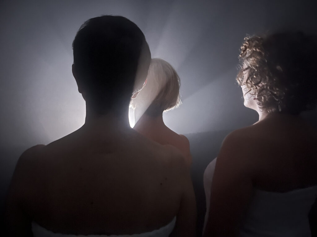 tre donne di spalle in ombra con indosso un asciugamano bianco